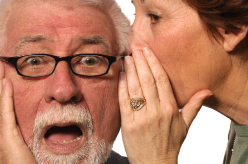 wife whispering in husbands' ear about reverse mortgages.